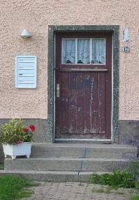 Die rostbraune Farbe bltterte von der hlzernen Tr der Nummer 17. Die Haustr entstammte noch einer anderen Zeit, hatte im oberen Drittel ein Fenster und war von innen mit einer gehkelten Gardine behangen. [Photo by Tom Keller]